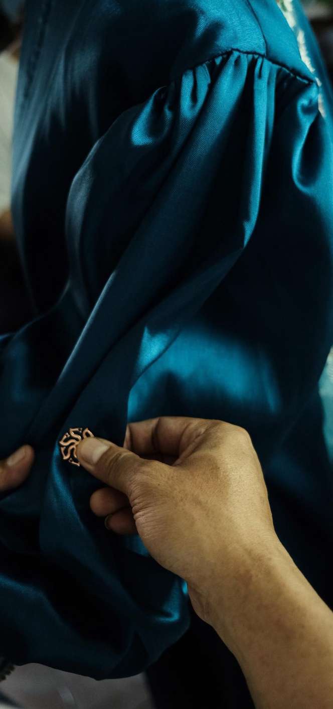 Hands carefully embellishing teal fabric in the atelier